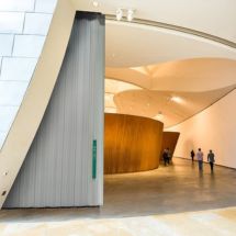 Modern architectural interior with curved walls, a high ceiling, and seamlessly integrated commercial door installation. A few people walk along the spacious, minimalist corridor with gray floors and light-colored walls.