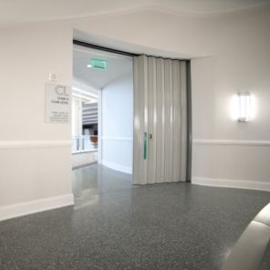 A partially open, accordion-style door on a glossy, gray-tiled floor with a wall-mounted light above it in a hallway.