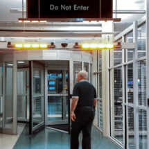 A man stands in front of a revolving door under a "Do Not Enter" sign with yellow warning lights illuminated above the entrance, highlighting the need for prompt automatic door repair services.