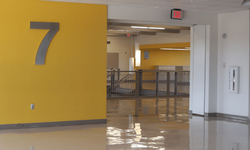 A hallway with a large number 7 on a yellow wall, polished floor, railing, and exit signs in a modern building featuring sleek commercial doors.